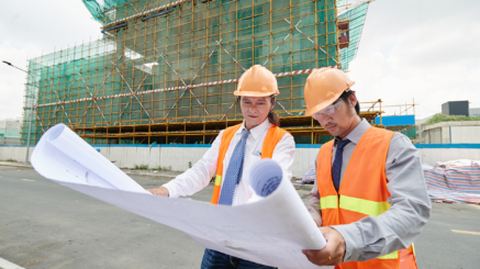 Asian engineers examining plan of building at the construction site