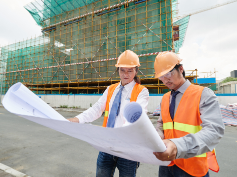 Asian engineers examining plan of building at the construction site